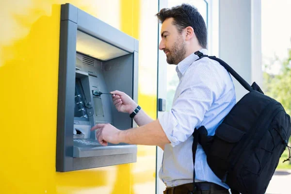 Férfi bankautomatánál áll, és az automatát használja.